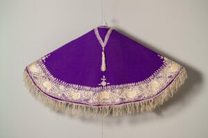 Purple cape with white embroidery and fringing.
