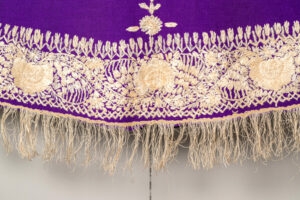 Close up detail of white embroidery and fringing on purple cape.