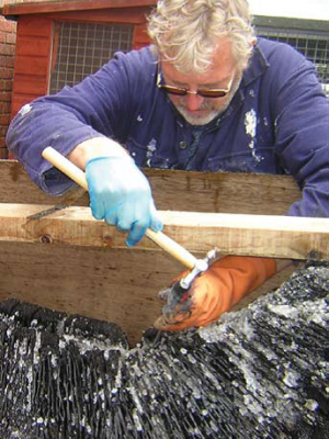 Photo of a man using a tool to remove salt crystals from the logboat.